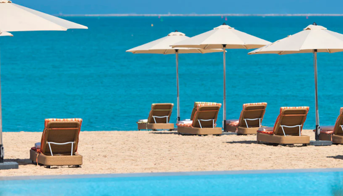 Marsa Malaz Kempinski Beach lounge chairs under umbrellas with a view of the turquoise sea.