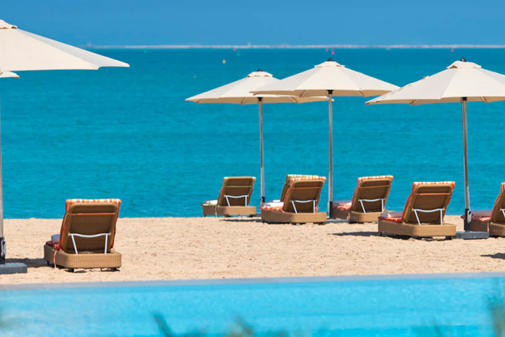 Beach lounge chairs under umbrellas with a view of the turquoise sea.