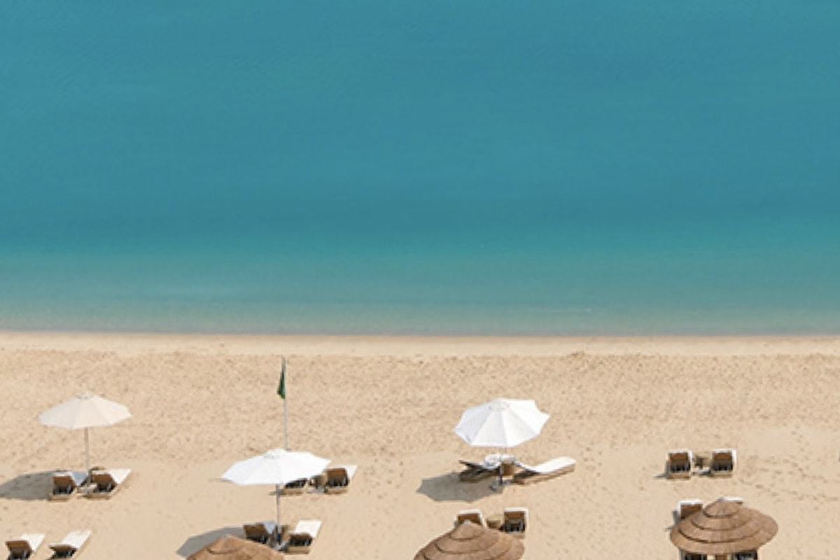A view of a beach with umbrellas and lounge chairs, overlooking the blue ocean under clear skies.