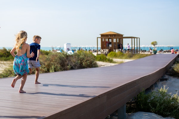 Children running along a wooden path towards a beach pavilion.