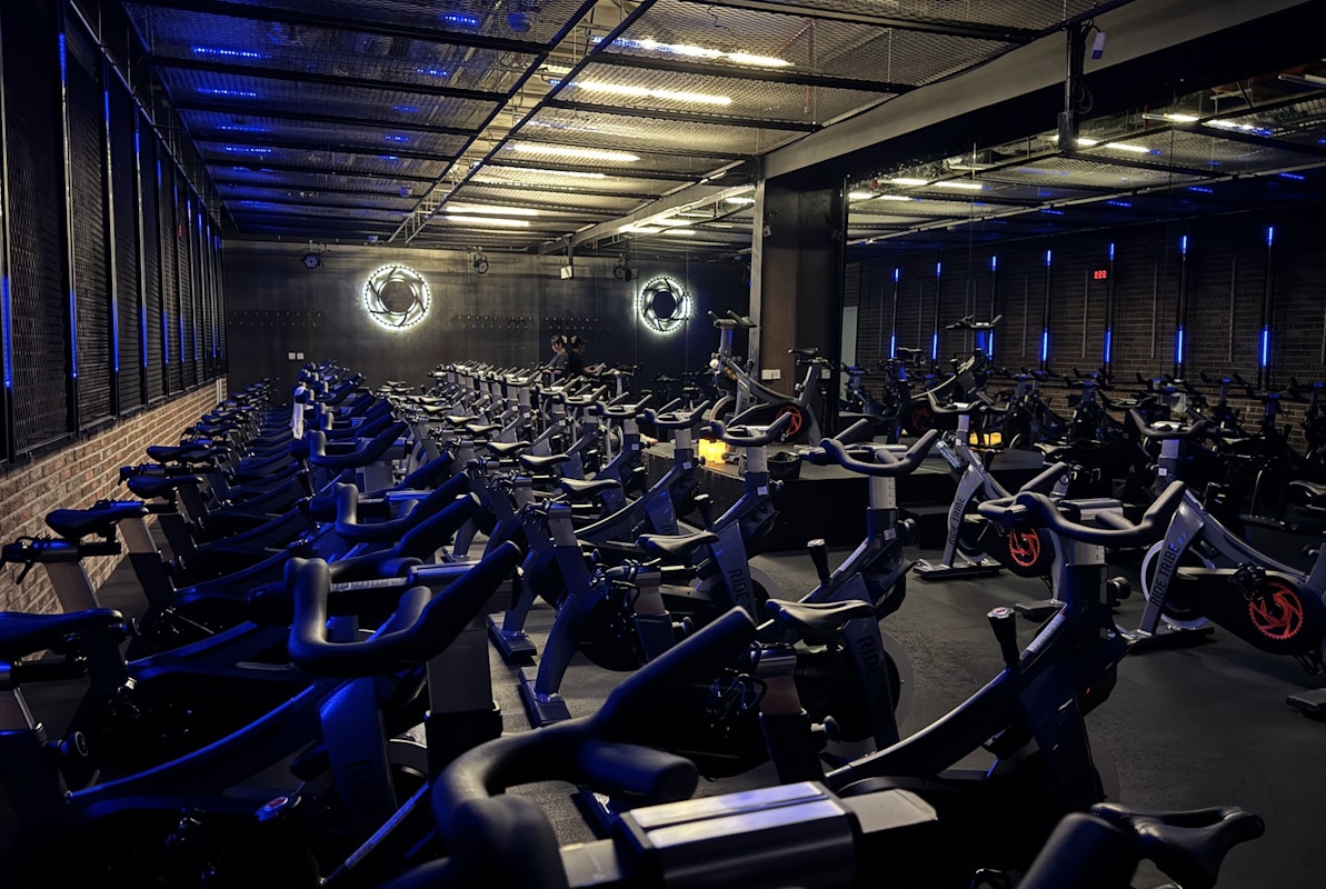 Spinning studio with rows of stationary bikes, blue neon lights, and industrial-style decor.