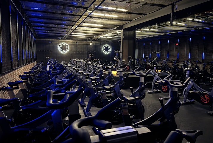 Spinning studio with rows of stationary bikes, blue neon lights, and industrial-style decor.