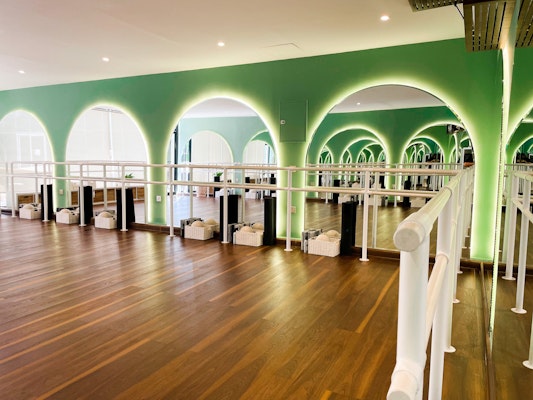 Modern dance studio with green arches, wooden flooring, and mirrored walls
