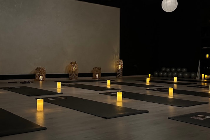 A peaceful yoga studio with dim lighting, soft candles placed on the floor near yoga mats, and decorative lamps creating a calm and serene atmosphere.