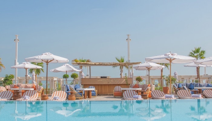 Bagatelle Beach Club Doha Outdoor pool with lounge chairs, umbrellas, and a bar area, surrounded by clear blue skies