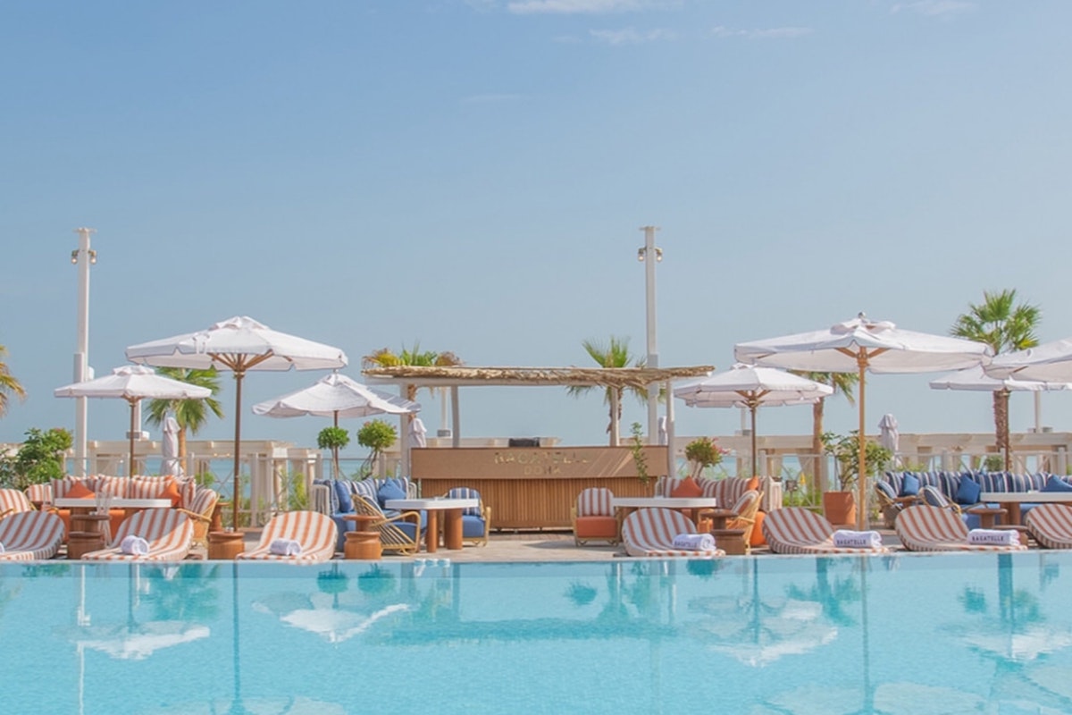 Outdoor pool with lounge chairs, umbrellas, and a bar area, surrounded by clear blue skies