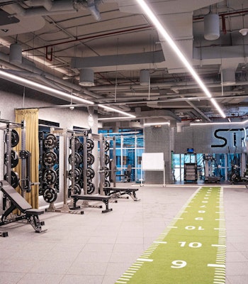 Ox Fitness Lab Modern gym with weightlifting equipment, a green fitness track, and bright industrial lighting.