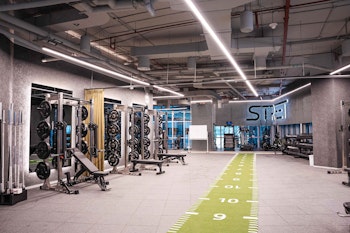 Modern gym with weightlifting equipment, a green fitness track, and bright industrial lighting.
