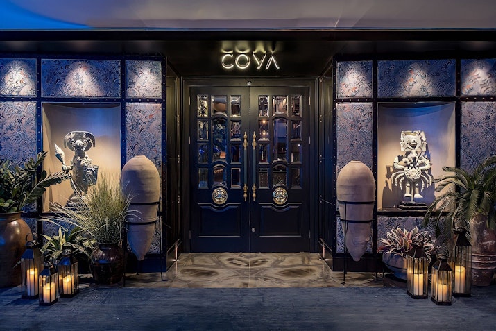 Elegant restaurant entrance with decorative plants, sculptures, and soft lighting.