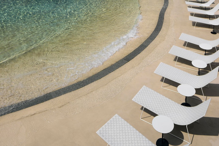 Beachside lounge chairs with white tables, overlooking the clear water