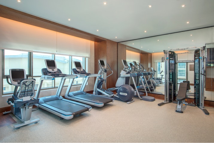 Well-lit gym with treadmills, ellipticals, and a multi-functional machine.