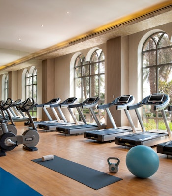 Marsa Malaz Kempinski Health Club Gym with exercise machines and equipment near large windows.