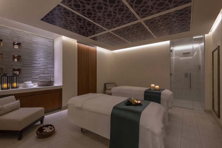 Wind down at M|SPA Calming spa treatment room with two massage tables, candles, and soft lighting.