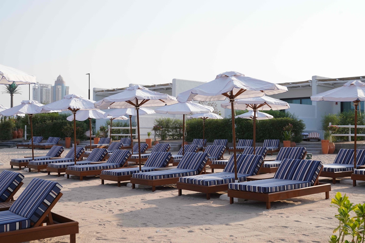 Bagatelle Beach Club Doha Beachside lounge chairs with striped cushions and umbrellas, arranged on the sand.