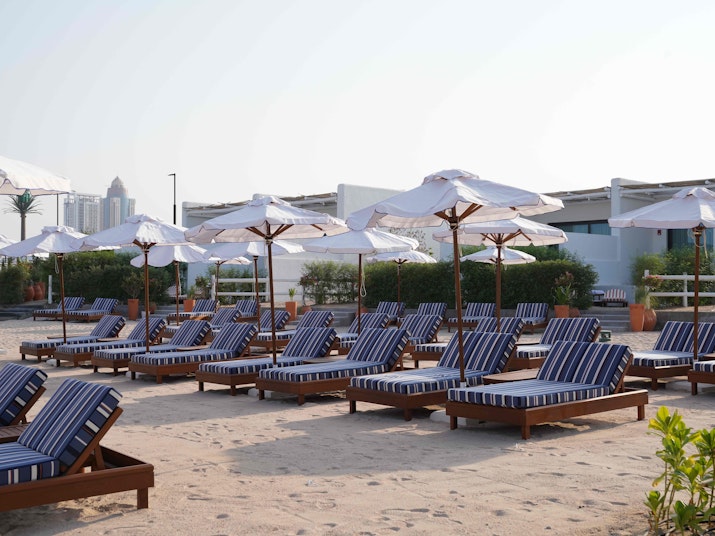 Beachside lounge chairs with striped cushions and umbrellas, arranged on the sand.