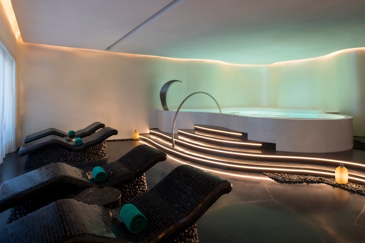 Luxurious spa room with curved lounge chairs, ambient lighting, and a circular Jacuzzi.