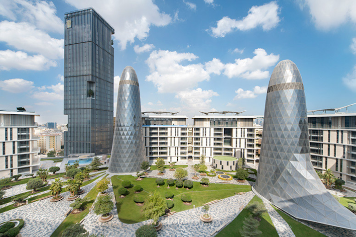 Modern architecture featuring a combination of futuristic tall buildings and unique conical structures, surrounded by landscaped greenery.