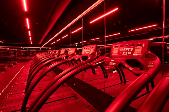 Red-lit gym with rows of treadmills and mirrors.