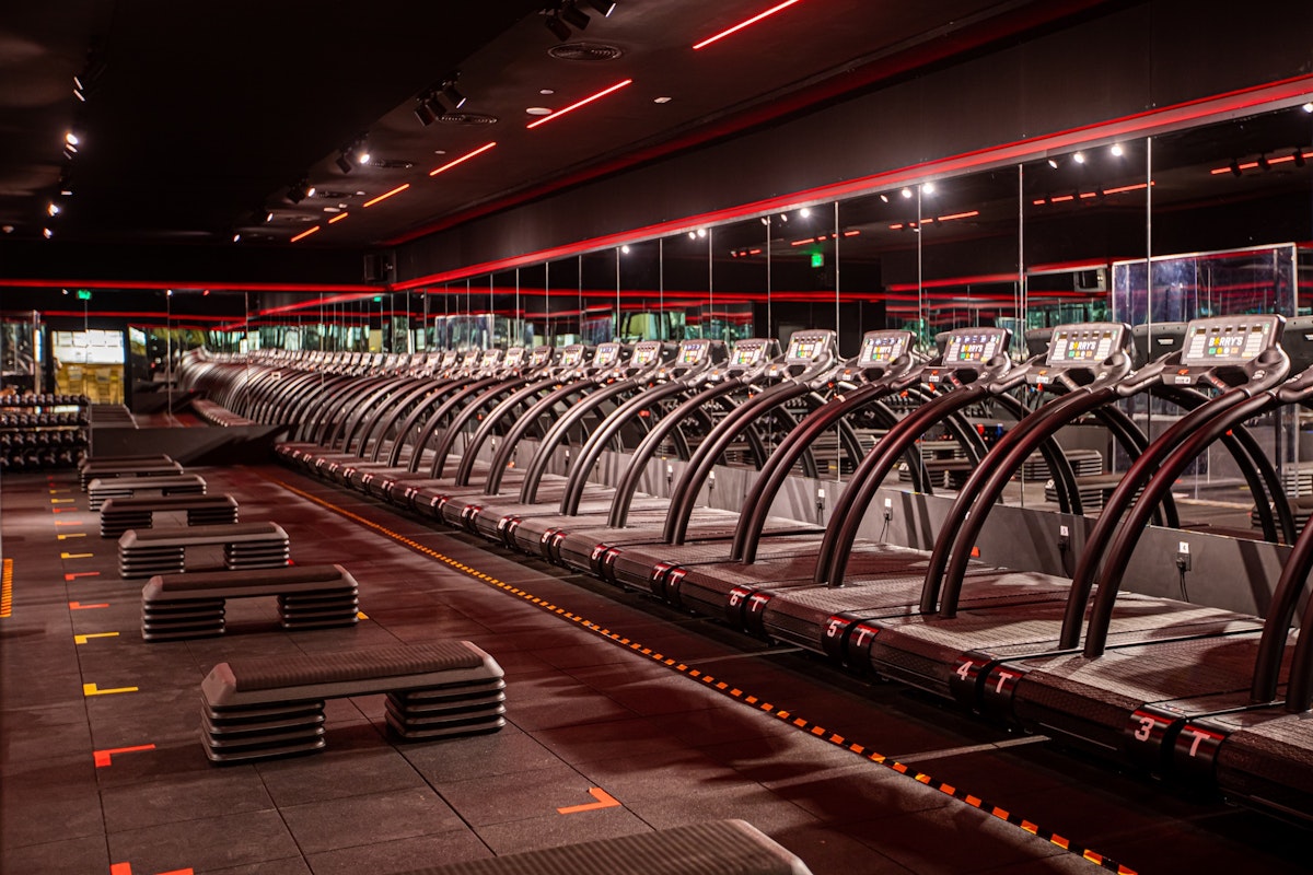 Gym with rows of treadmills, exercise benches, and red ambient lighting