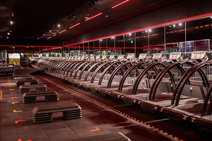 Gym with rows of treadmills, exercise benches, and red ambient lighting