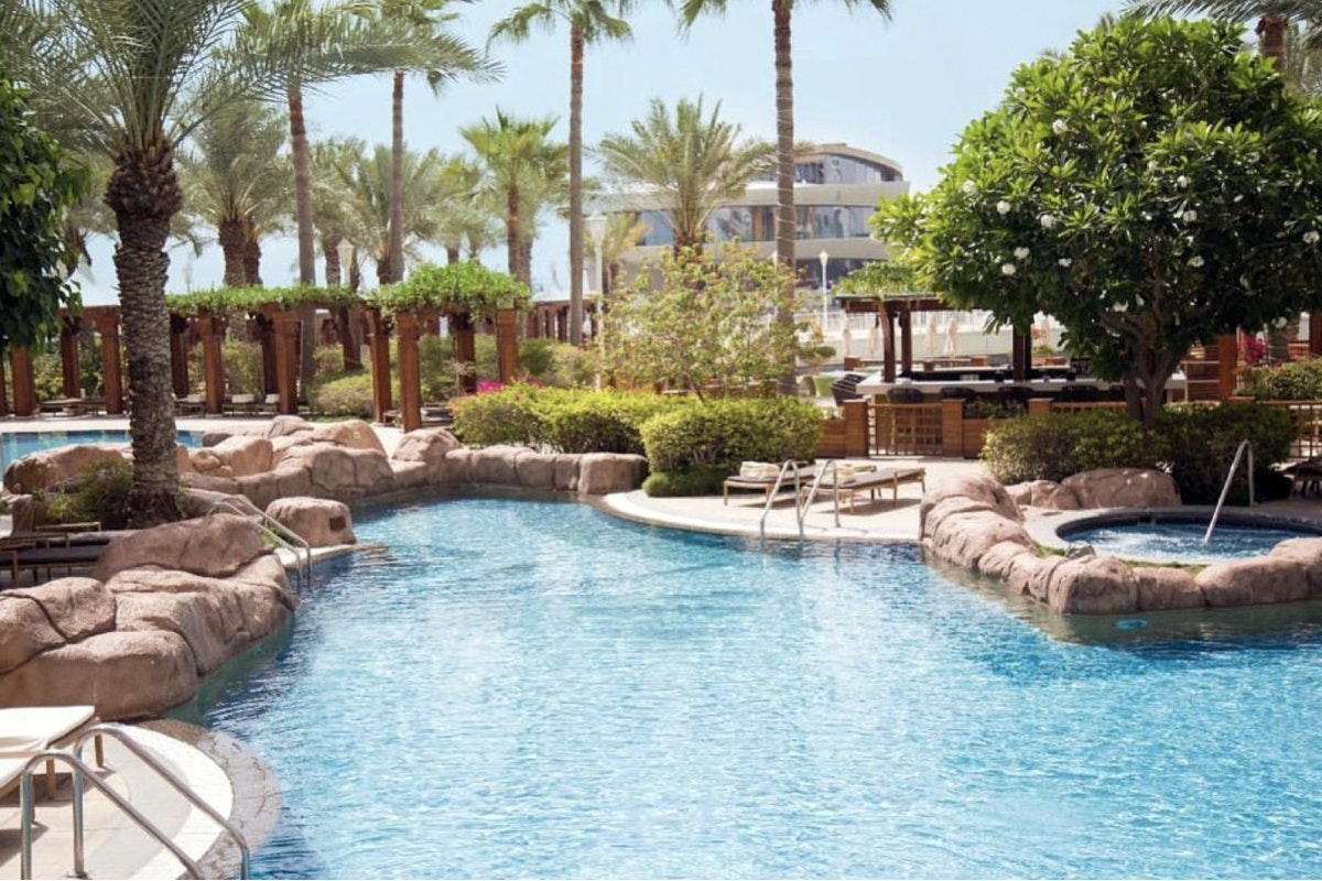 Four Seasons Hotel Doha Resort pool with rock features, palm trees, and tropical landscaping