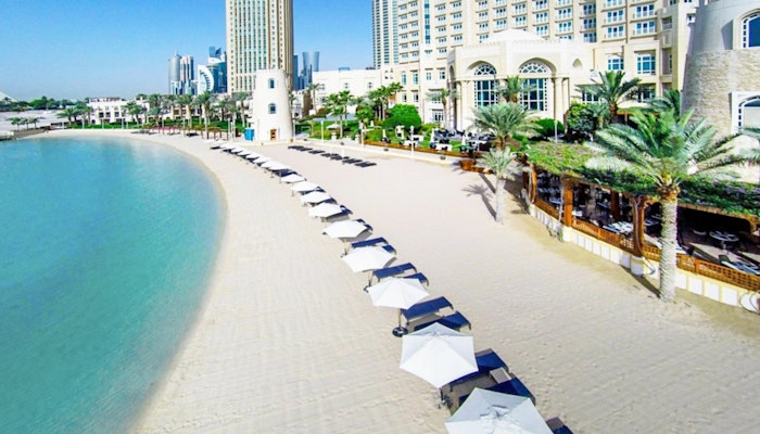 Four Seasons Hotel Doha Beach with rows of umbrellas, clear water, and a resort building in the background