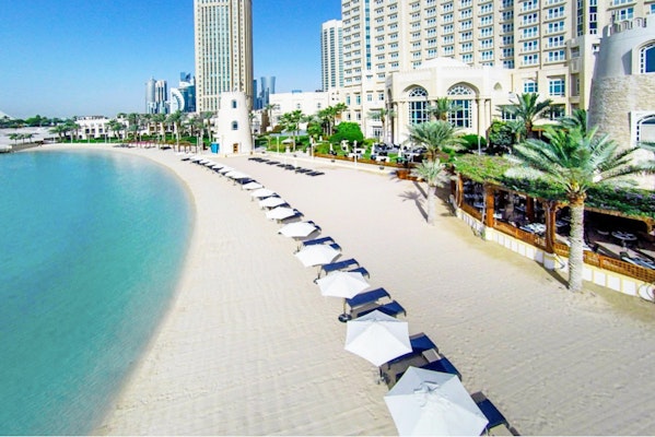 Beach with rows of umbrellas, clear water, and a resort building in the background