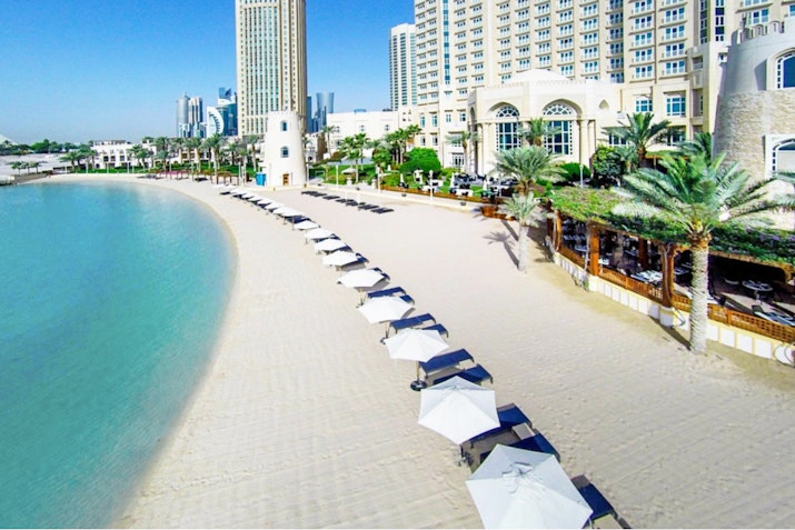 Beach with rows of umbrellas, clear water, and a resort building in the background