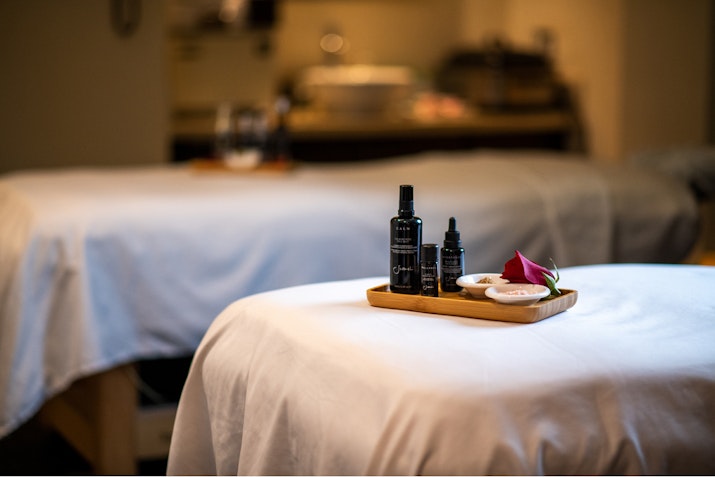 Spa treatment room with massage tables and essential oils on a wooden tray.