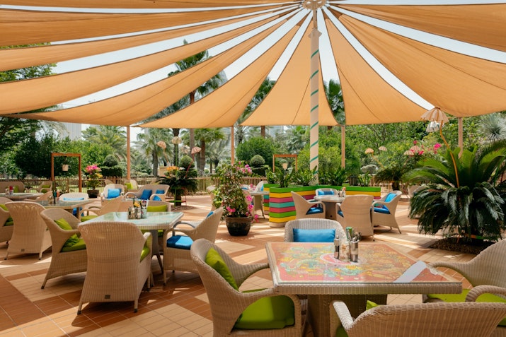 Outdoor dining area with colorful chairs and a large canopy, surrounded by lush plants.