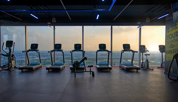 Gymmito Lusail Modern gym with treadmills and elliptical machines, with a scenic view of the ocean at sunset.