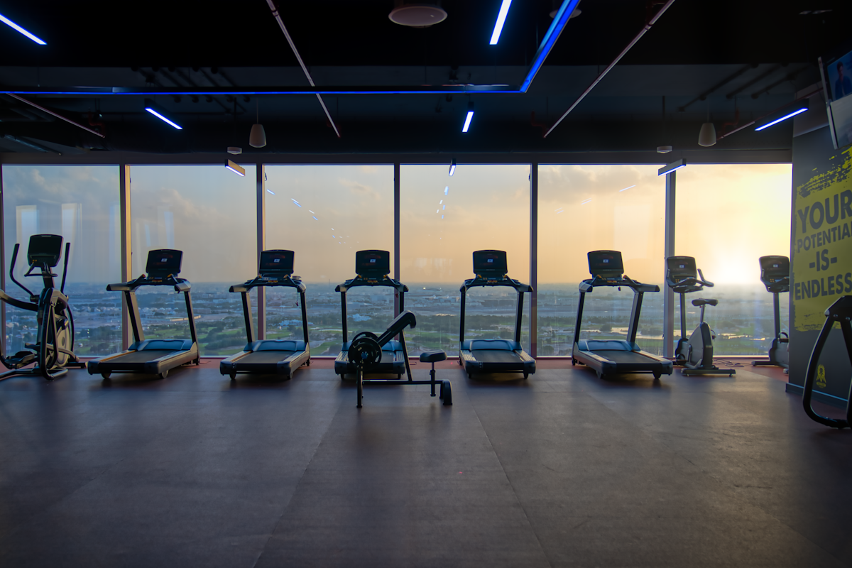 Gymmito Lusail Modern gym with treadmills and elliptical machines, with a scenic view of the ocean at sunset.