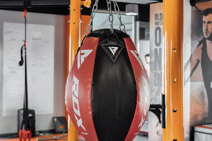 Gymmito Heavy punching bag hanging in a gym, with red and black panels and RDX branding.