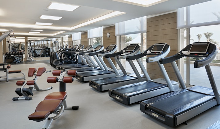 Modern gym with treadmills, weight benches, and large windows letting in natural light.