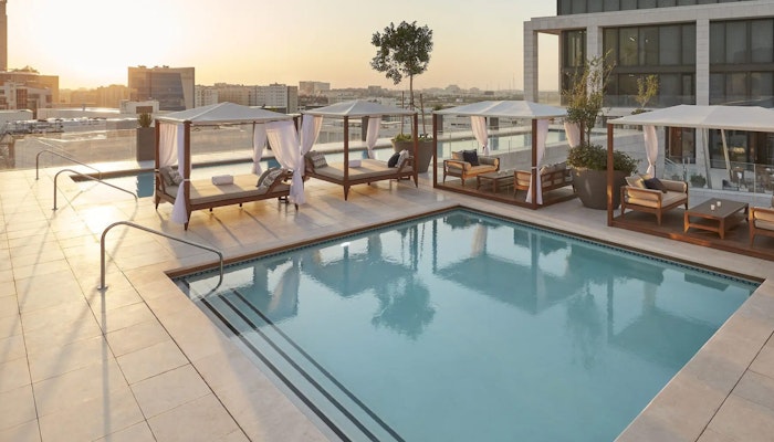 Mandarin Oriental, Doha Rooftop pool with cabanas and city skyline in the background at sunset.