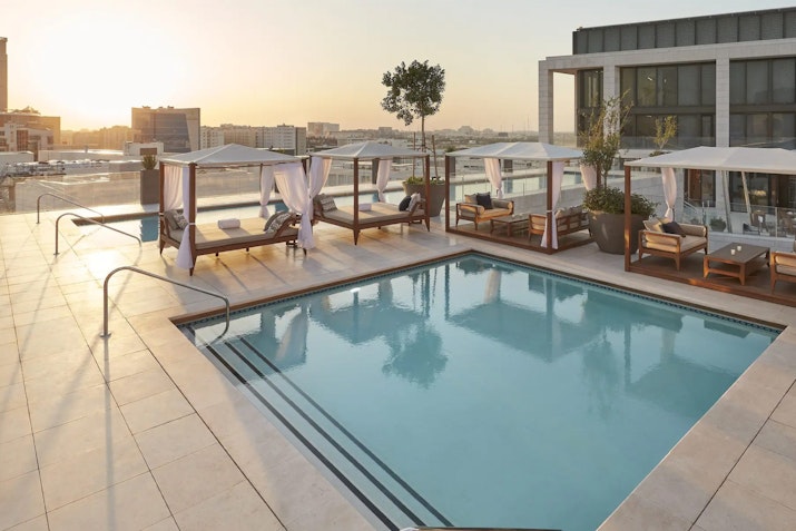 Rooftop pool with cabanas and city skyline in the background at sunset.