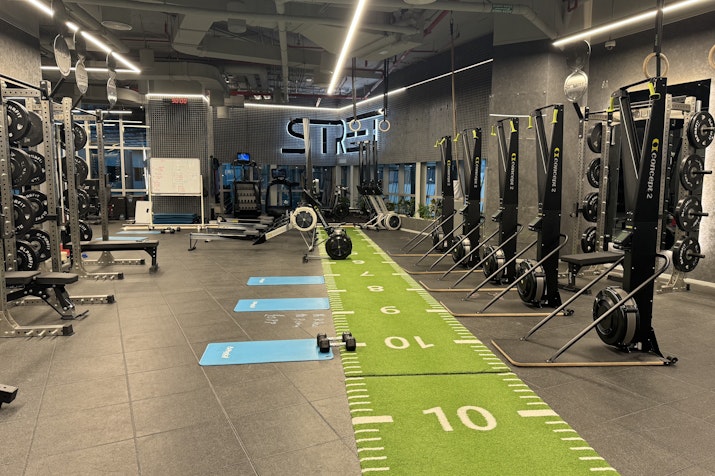 Modern gym with weightlifting equipment, suspension trainers, and a green turf track for fitness activities.