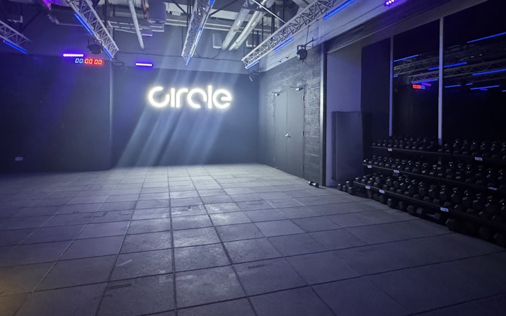 Circle a 360-degree Fitness Experience Fitness studio with a neon 'Circle' sign, dumbbell racks, and dramatic lighting.