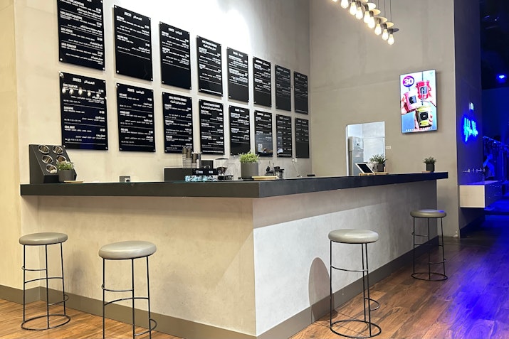 Modern café counter with stools, menu boards, and a TV screen