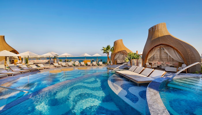 SUSHISAMBA Doha A luxurious pool area with cabanas, lounge chairs, and a clear blue sky overlooking the sea.