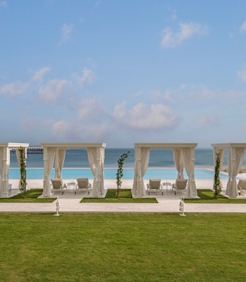 The Chedi Katara Hotel & Resort Outdoor seating area with white cabanas overlooking a beach and ocean.