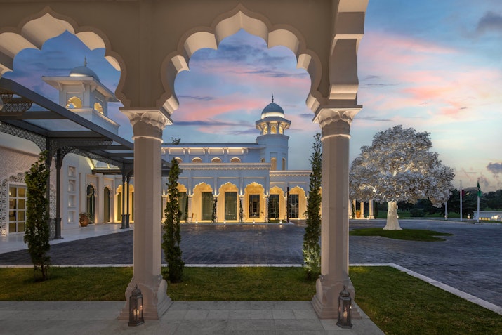 Archway view of a grand building at sunset with a landscaped garden.
