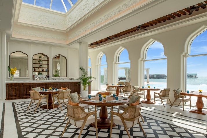 The Chedi Katara Hotel & Resort Elegant dining area with tables, chairs, and large windows overlooking the beach.