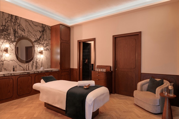 Luxury spa treatment room with a massage table, marble vanity, and elegant wooden furniture.