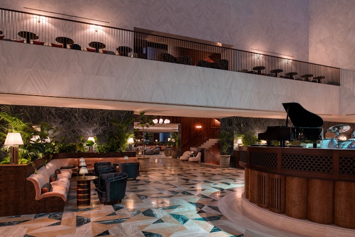 Elegant hotel lobby with a grand piano, luxurious seating, and a beautiful marble floor design.