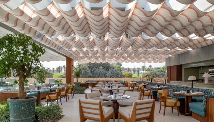 Malibu Kitchen at The Ned Doha Stylish outdoor dining area with a unique ceiling design, wooden furniture, and lush greenery.