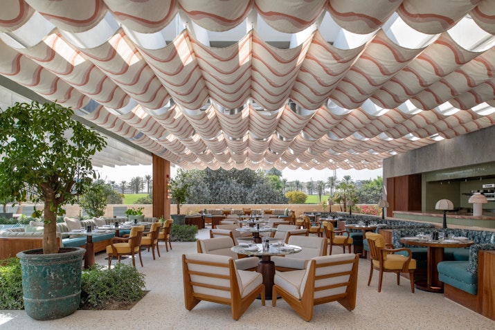Stylish outdoor dining area with a unique ceiling design, wooden furniture, and lush greenery.