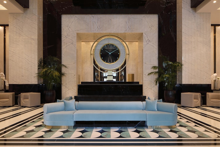 Luxurious hotel lobby with a large round mirror, a blue sofa, and elegant marble flooring