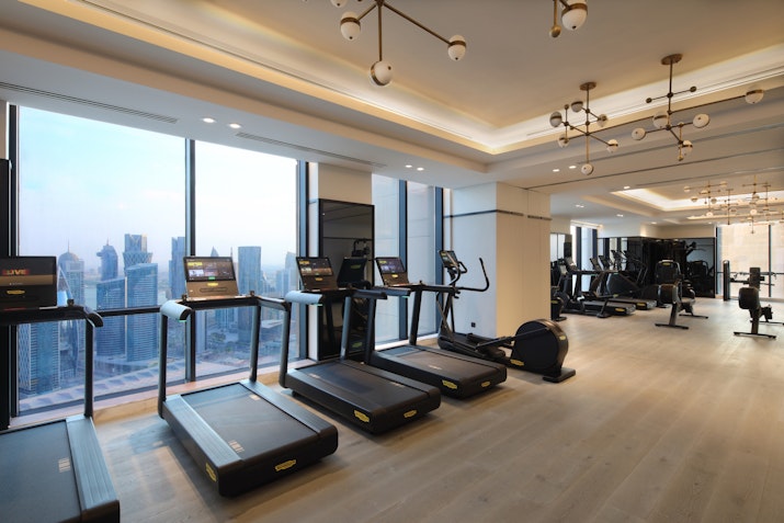 Modern gym with treadmills and cardio machines, offering city skyline views through large windows