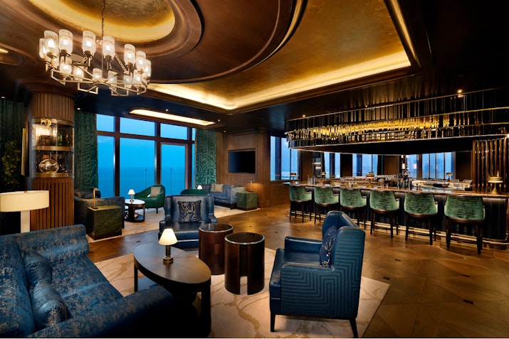 Elegant bar lounge with plush seating, a well-lit bar, and a view of the ocean.
